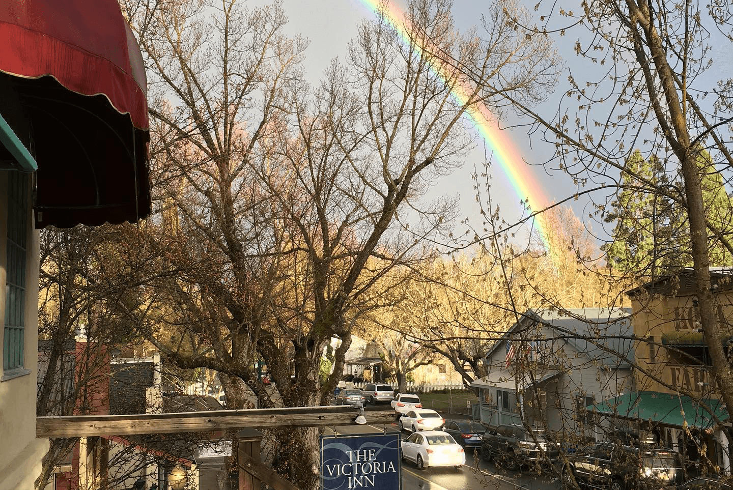 A rainbow stretches over a neighborhood scene with bare trees and a sign for The Victoria Inn.