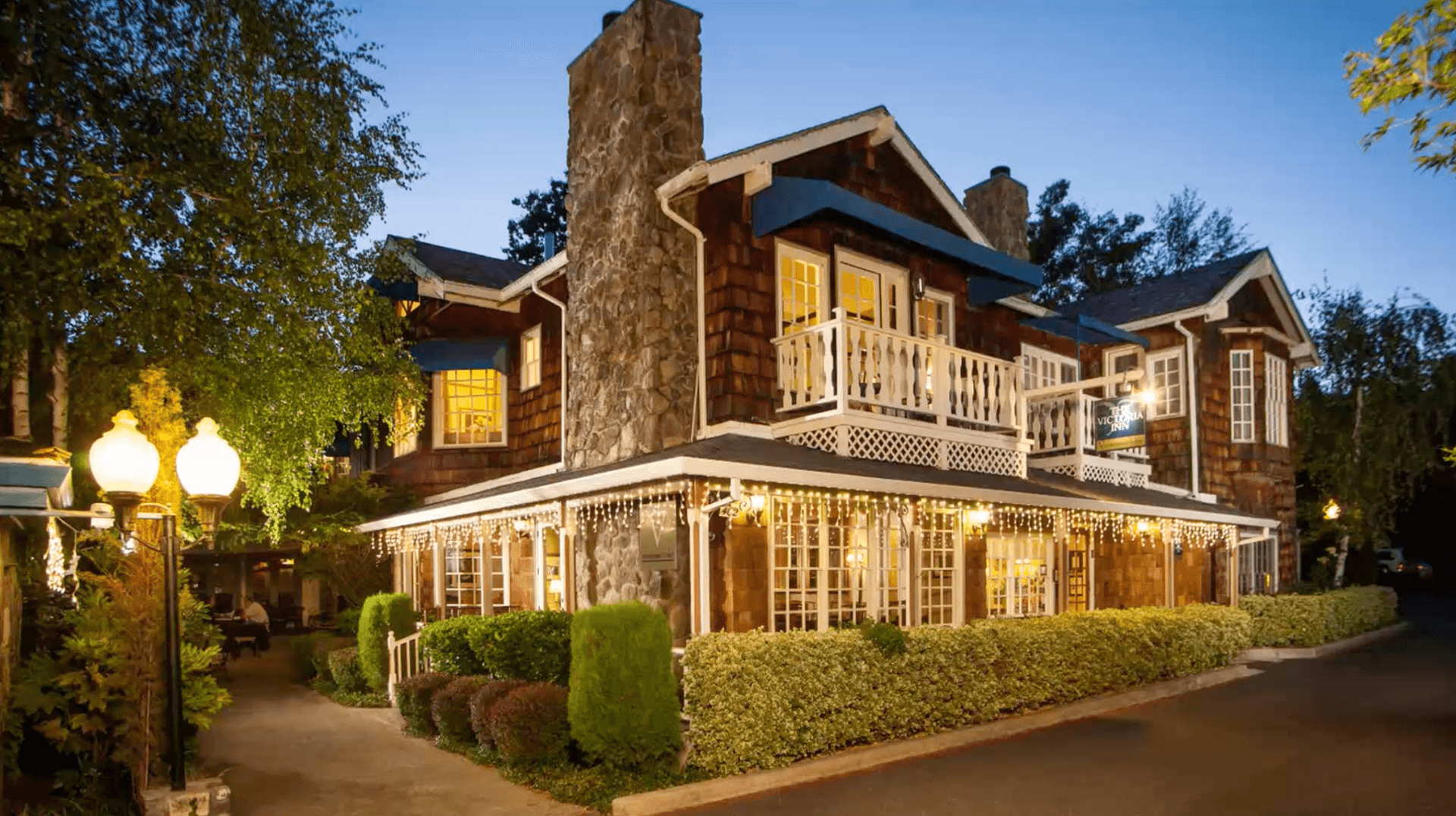 Charming two-story wooden building with a stone chimney, softly illuminated at dusk.