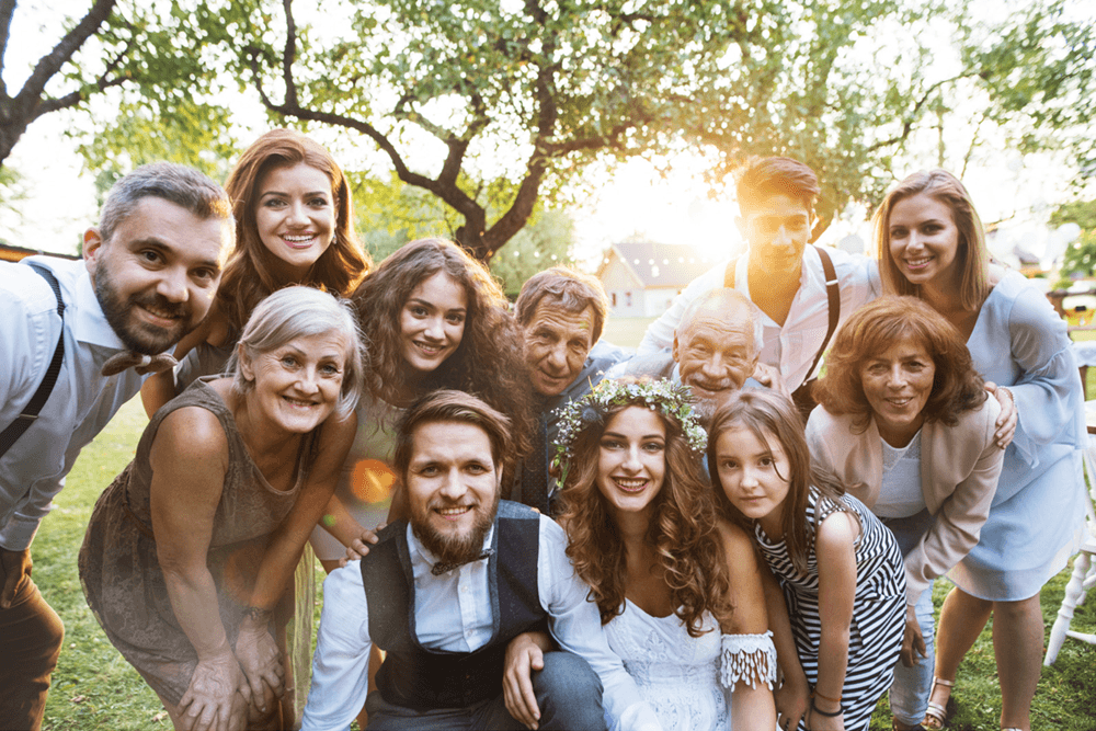 A joyful group of family and friends poses together outdoors for a wedding celebration.