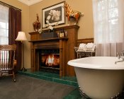 Tan room and fireplace with wood mantle surround, a wood rocking chair, and white freestanding tub