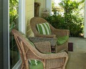 Covered patio with white railing, two wicker chairs with green cushions and green and white striped pillows