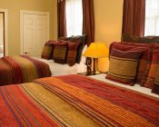 Bedroom with two beds covered in red and gold striped bedspreads, a nightstand, and two large windows