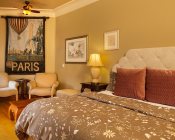 bedroom with tan colored paisley comforter, red pillows, night stand with lamp, pictures on wall and Paris Banner