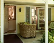 Covered patio with two wicker loveseats with green and white cushions in front of a partially open French door