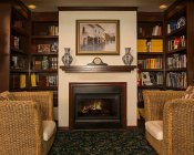 Charming nook with dark wood bookshelves flanking an fireplace with two wicker loveseats on a dark green floral rug